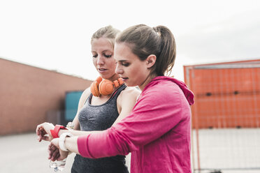 Zwei Frauen, die eine Pause vom Sport machen und auf ihre Smartwatches schauen - UUF10929
