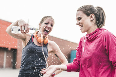 Zwei verspielte Frauen mit Wasserflasche, die eine Pause vom Sport machen - UUF10931