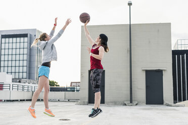 Zwei Frauen spielen Basketball auf einem Parkdeck in der Stadt - UUF10942