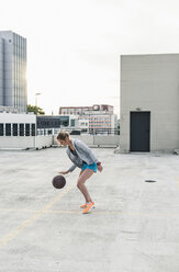 Frau spielt Basketball auf einem Parkdeck in der Stadt - UUF10946