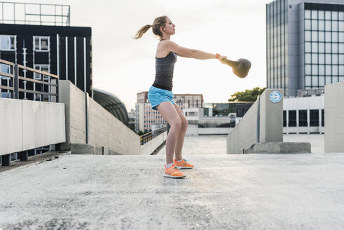 Frau beim Training mit einer Kettlebell auf einem Parkdeck in der Stadt - UUF10949