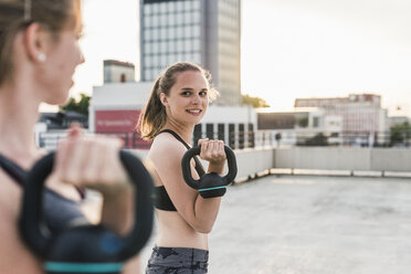 Two women exercising with kettlebells on parking level in the city - UUF10951