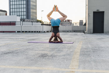 Woman doing a headstand on parking level in the city - UUF10960