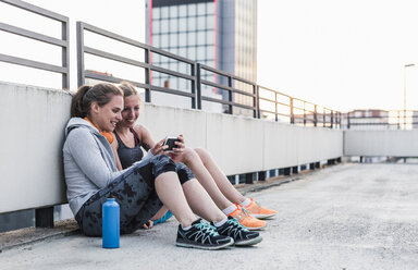 Zwei Frauen, die eine Pause vom Sport machen und ihr Smartphone teilen - UUF10967