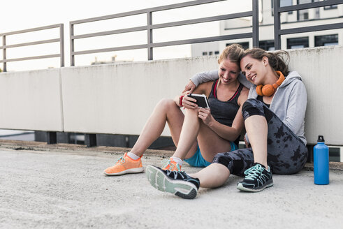 Zwei Frauen, die eine Pause vom Sport machen und ihr Smartphone teilen - UUF10968