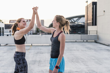 Zwei glückliche Frauen, die auf einem Parkdeck in der Stadt eine Pause vom Sport machen - UUF10969