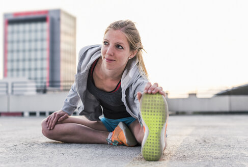 Aktive Frau beim Stretching auf einem Parkdeck in der Stadt - UUF10970