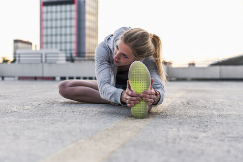 Aktive Frau beim Stretching auf einem Parkdeck in der Stadt - UUF10971