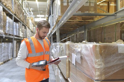 Man in factory hall wearing safety vest holding clipboard and barcode scanner stock photo