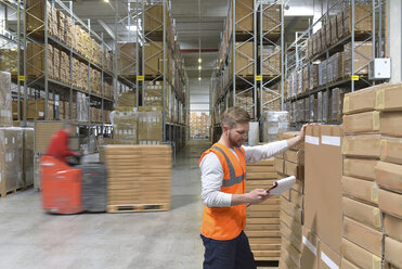 Man with clipboard in factory hall and moving forklift - LYF00742