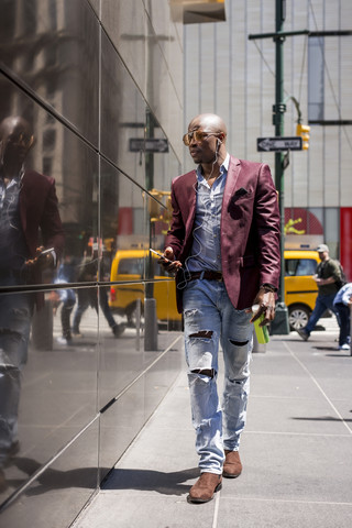 USA, New York City, Manhattan, stilvoller Geschäftsmann hört Musik mit Kopfhörern und Smartphone, lizenzfreies Stockfoto