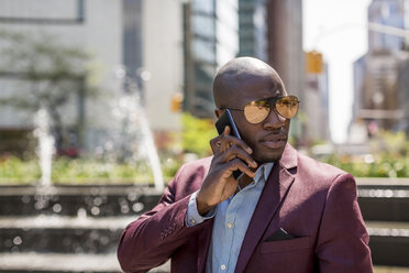 USA, New York City, Manhattan, portrait of businessman wearing mirrored sunglasses on the phone - MAUF01142