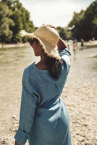 Frau mit Strohhut und Jeanskleid am Strand, lizenzfreies Stockfoto