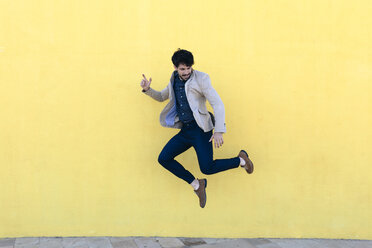 Junger Mann, der vor einer gelben Wand in die Luft springt - GIOF02874