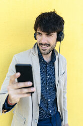 Porträt eines jungen Mannes mit Kopfhörern und Mobiltelefon - GIOF02878