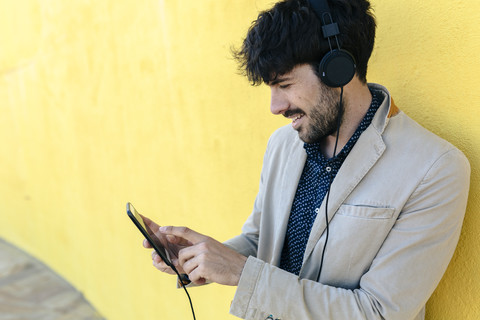 Lächelnder junger Mann mit Kopfhörern und Mobiltelefon, lizenzfreies Stockfoto