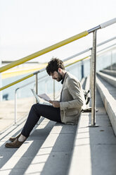 Pensive man sitting on steps outdoors checking documents - GIOF02885