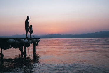 Italien, Lazise, Vater und kleine Tochter stehen auf einem Steg und schauen auf den Gardasee bei Sonnenuntergang - IPF00394