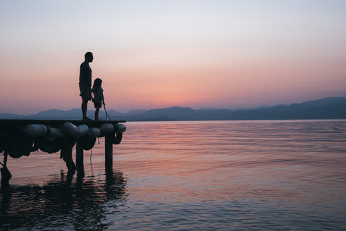 Italy, Lazise, father and little daughter standing on jetty looking at Lake Garda at sunset - IPF00394