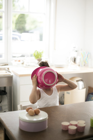 Little girl in kitchen covering her face with pink mixing bowl stock photo