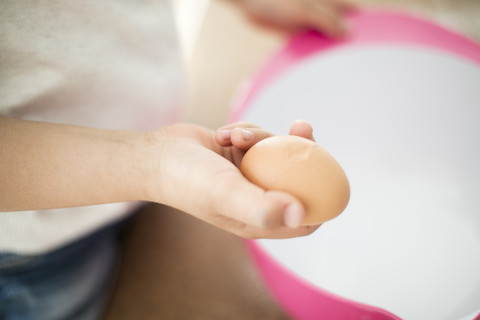 Mädchenhand hält aufgeschlagenes Ei, Nahaufnahme, lizenzfreies Stockfoto