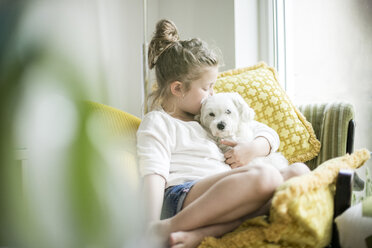 Kleines Mädchen sitzt auf einem Sessel zu Hause und kuschelt mit ihrem Hund - MOEF00054