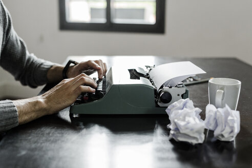 Nahaufnahme eines Mannes, der eine Schreibmaschine mit zerknittertem Papier auf dem Schreibtisch benutzt - GIOF02890