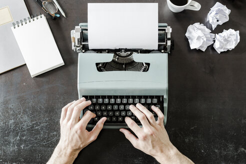 Nahaufnahme eines Mannes, der eine Schreibmaschine mit zerknittertem Papier auf dem Schreibtisch benutzt - GIOF02892