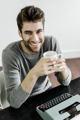 Portrait of smiling young man with typewriter - GIOF02893