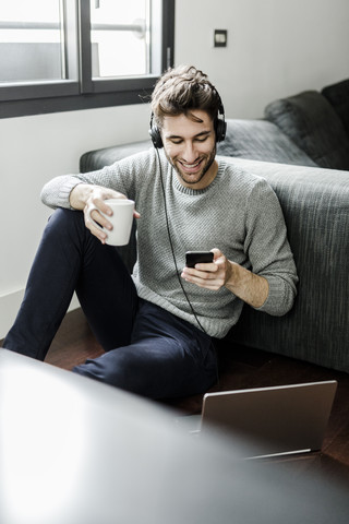 Smiling young man with cell phone, laptop and headphones at home stock photo