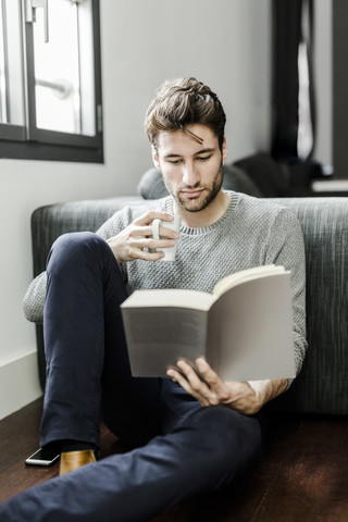 Junger Mann liest zu Hause ein Buch, lizenzfreies Stockfoto