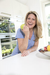 Porträt einer glücklichen Frau, die zu Hause einen Apfel isst - MAEF12239