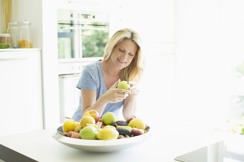 Smiling woman at home taking apple from fruit bowl stock photo