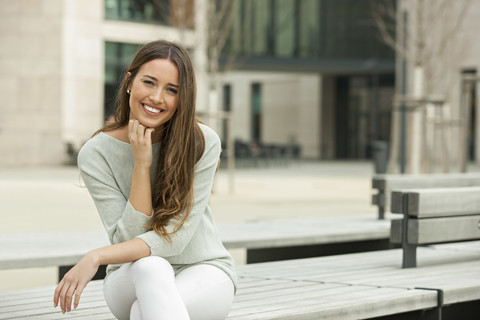 Junge Frau auf einer Bank sitzend, lächelnd, lizenzfreies Stockfoto