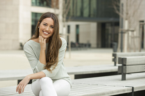 Junge Frau auf einer Bank sitzend, lächelnd - CHAF01899
