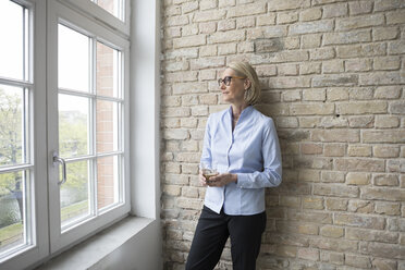 Mature businesswoman looking out of window, holding cup of coffee - RBF05768