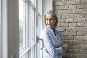 Mature businesswoman standing at window, looking worried - RBF05771