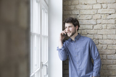 Young businessman standing at window, using smartphone - RBF05804