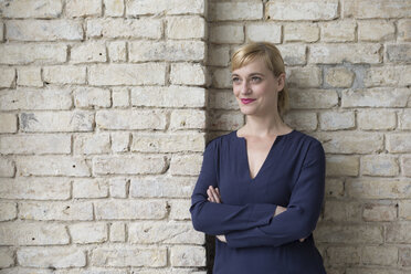 Businesswoman leaning against brick wall, looking away - RBF05829