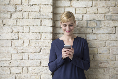 Geschäftsfrau lehnt an einer Backsteinmauer und benutzt ein Smartphone, lizenzfreies Stockfoto