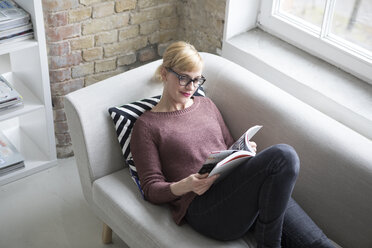 Woman sitting on couch, reading book - RBF05838