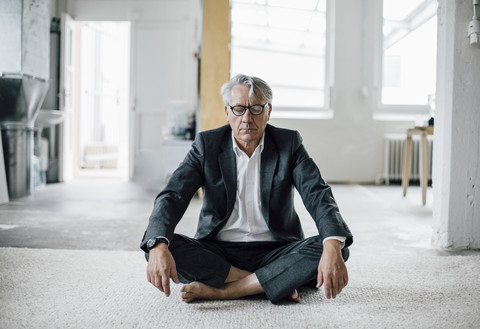 Senior businessman sitting on floor meditating stock photo