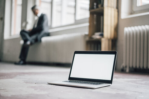 Laptop auf dem Boden mit Geschäftsmann im Hintergrund - GUSF00034