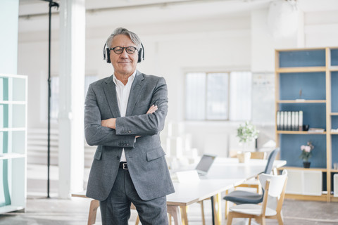 Älterer Geschäftsmann, der im Büro mit Kopfhörern Musik hört, lizenzfreies Stockfoto