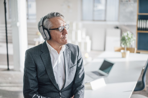 Älterer Geschäftsmann, der im Büro mit Kopfhörern Musik hört, lizenzfreies Stockfoto