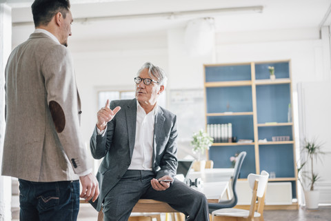 Senior businessman talking to young businessman in office stock photo