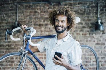 Lächelnder junger Mann mit Fahrrad und Mobiltelefon - KNSF01712