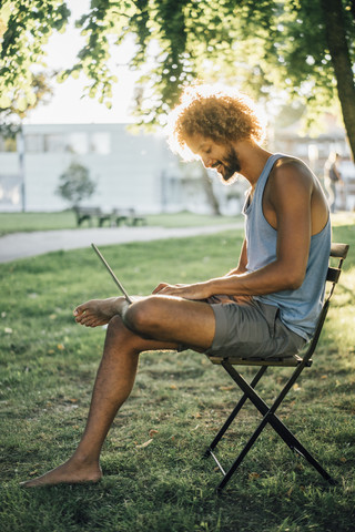 Man with beard and curly hair using laptop in park stock photo