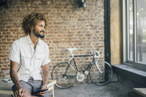 Lächelnder junger Mann mit Tablet und Fahrrad im Hintergrund - KNSF01725