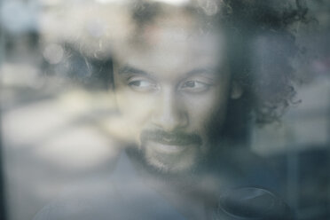 Man with beard and curly hair looking out of window - KNSF01729